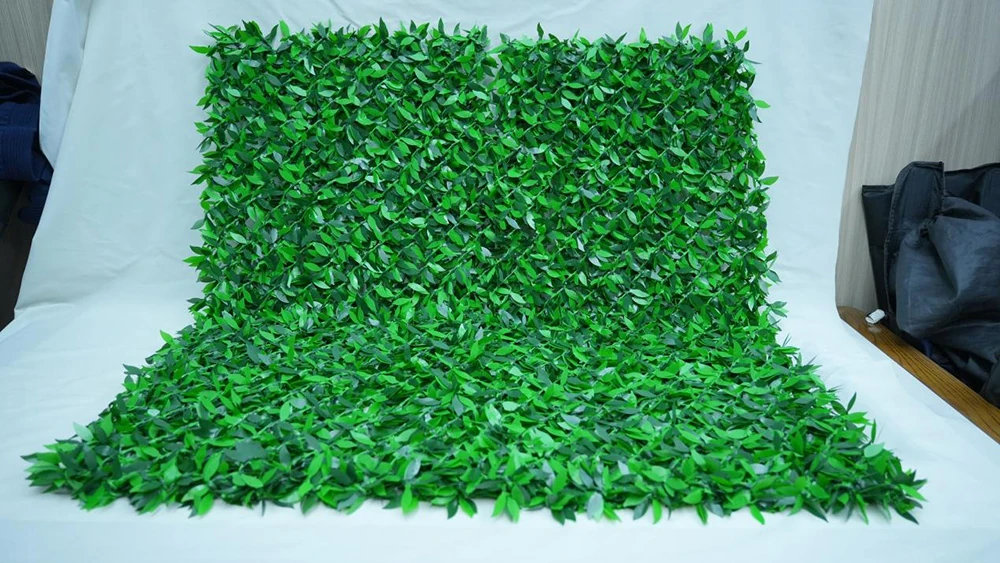 Green artificial leaf privacy hedge panel with grid backing laid flat on studio background