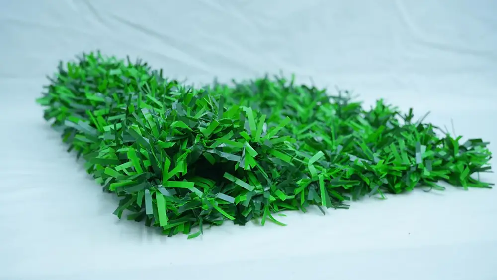 a rectangular panel of artificial green hedge with a dense texture of small plastic leaves lies flat on a white surface.
